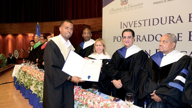 La maestra Denia Burgos entrega su diploma a uno de los graduandos. Junto a ella el rector Iván Grullón y otros funcionarios importantes de la UASD